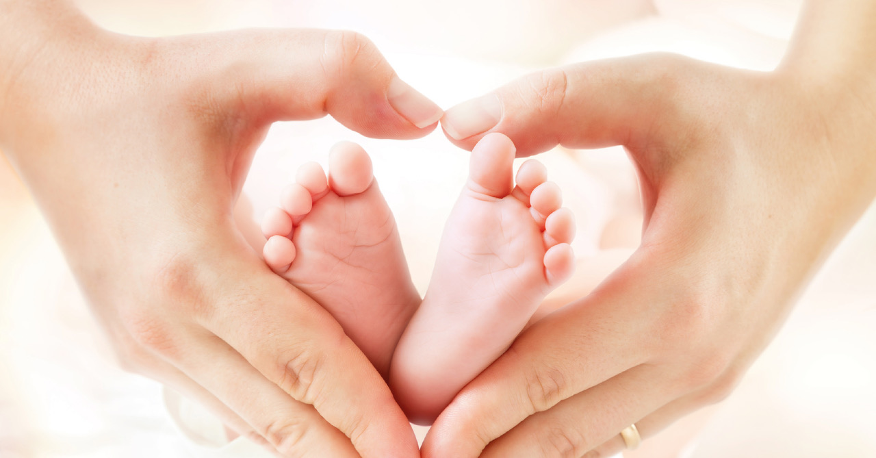 Kleine Babyfüsschen die von zwei Händen in herzförmiger Pose gahlten werden