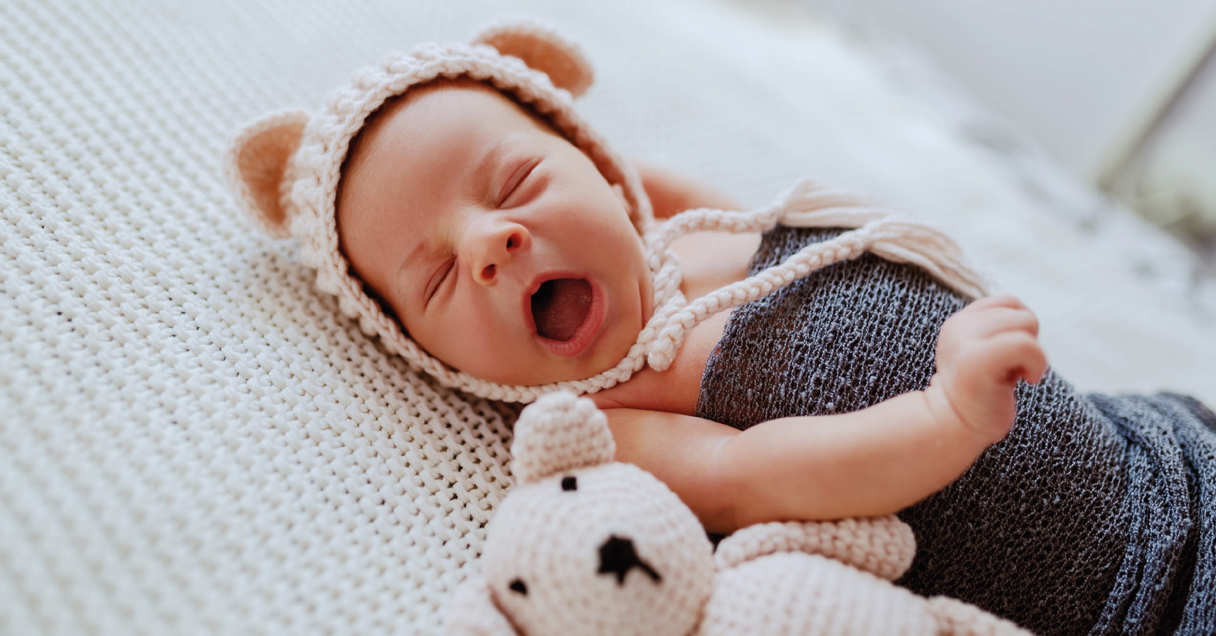 Ein müdes, gähnendes Baby mit Wollmützchen